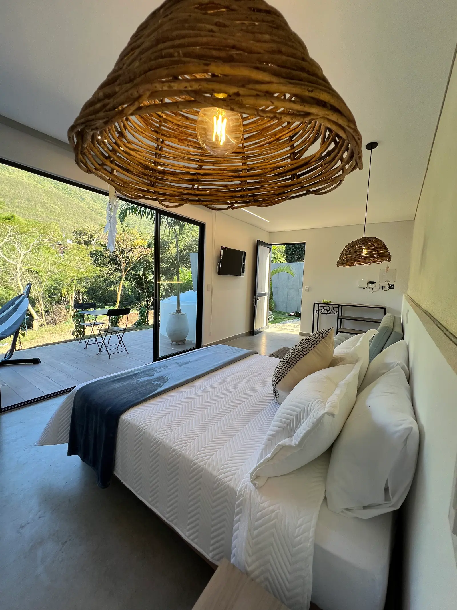 Cama de la cabaña Deluxe bajo lámparas de mimbre, con el jardín al otro lado del vidrio